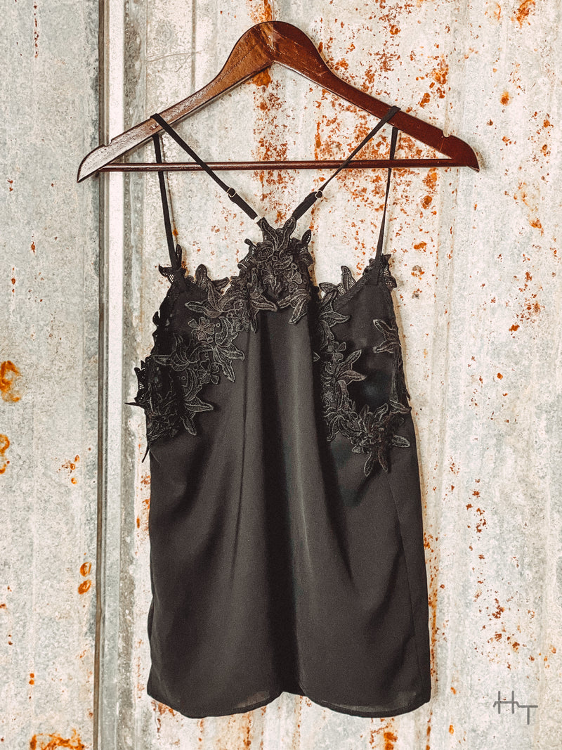 Photo of back of black cami with floral lace detail.  Hanging on hanger with tin background