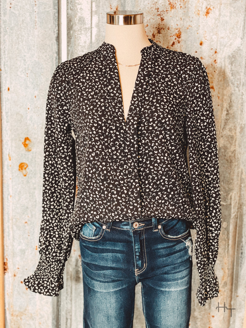 Photo of black v neck long sleeve top with small cream colored leopard print spots on a mannequin with tin background