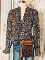 Photo of black v neck long sleeve top with small cream colored leopard print spots paired with brown leather and stamped leather purse on a mannequin with tin background