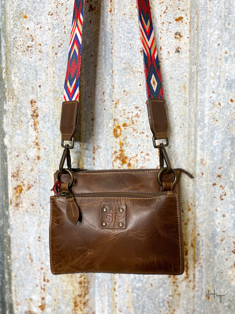 Photo of close up of body of dark brown leather with STS patch on front with aztec pattern multi color strap with tin background
