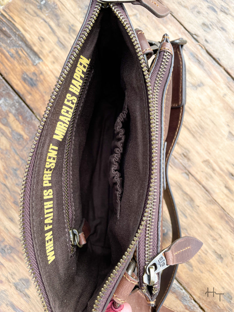 Photo of dark brown leather purses large zip pocket with inside zipper pocket an elastic slip pocket and quote printed on the inside "when faith is present miracles happen"