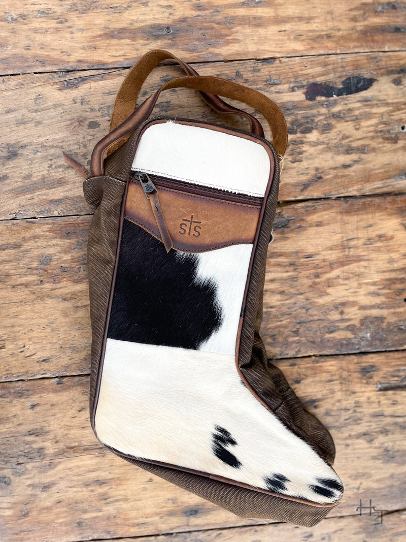 Photo of option B black and white cowhide and brown leather boot bag with front zipper pocket brown canvas sides and leather carrying handles with wood background