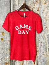 Photo of red tee shirt with words Game Day printed in white on front on a hanger with a tin background