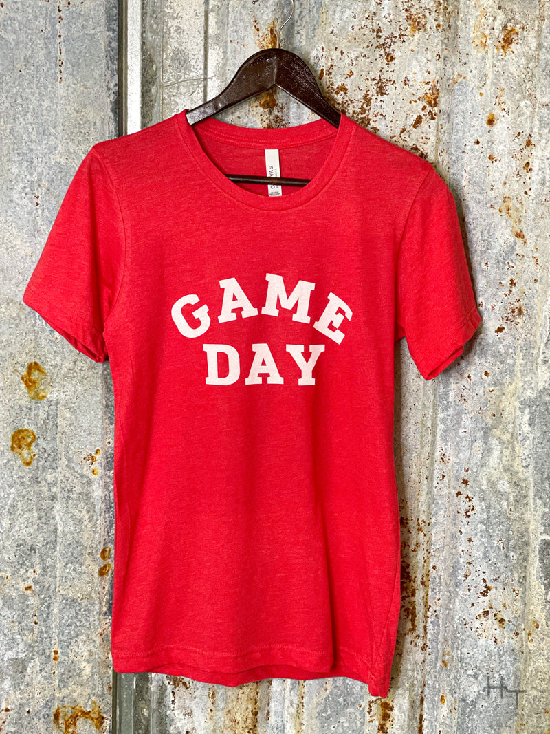 Photo of red tee shirt with words Game Day printed in white on front on a hanger with a tin background