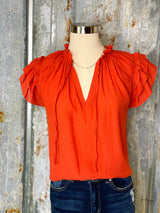 Photo of terra cotta red top with short ruffled sleeve and a v neck on a mannequin with a tin background