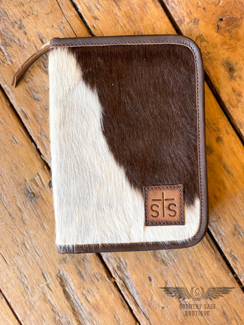 Dark brown and white cowhide front of jewelry case with leather STS patch with wood background
