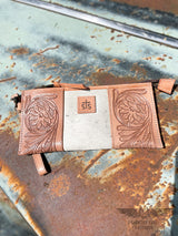 Image of the front side of option A of yipee kiyay clutch wallet with veggie tan leather that is stamped with a floral design on each side with white cowhide with faint black speckles in the middle with a leather patch with STS branded into it.  