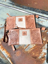 Image of 2 yipee kiyay clutch wallets that are veggie tan floral tooled leather and white speckled cowhide with leather patch with STS branded on it laying flat on a rusty truck hood.