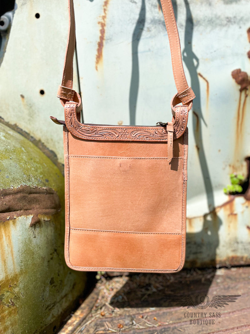 Image of back side of Yipee Kiyay crossbody purse.  Solid veggie tan leather with back pocket with magnetic closure and tooled leather detail on the top.  Zipper closure.